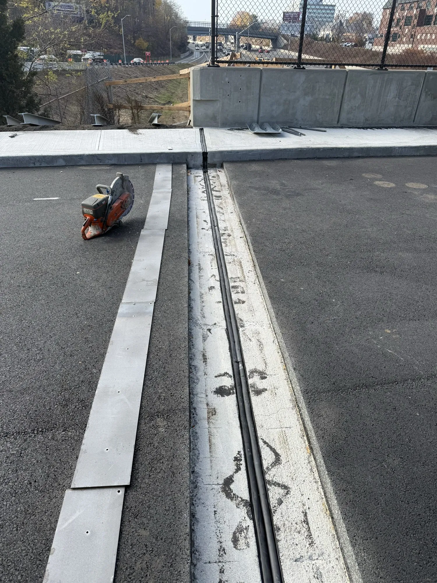 Sealed gutter-line joint along a bridge deck curb with a concrete saw and city skyline behind