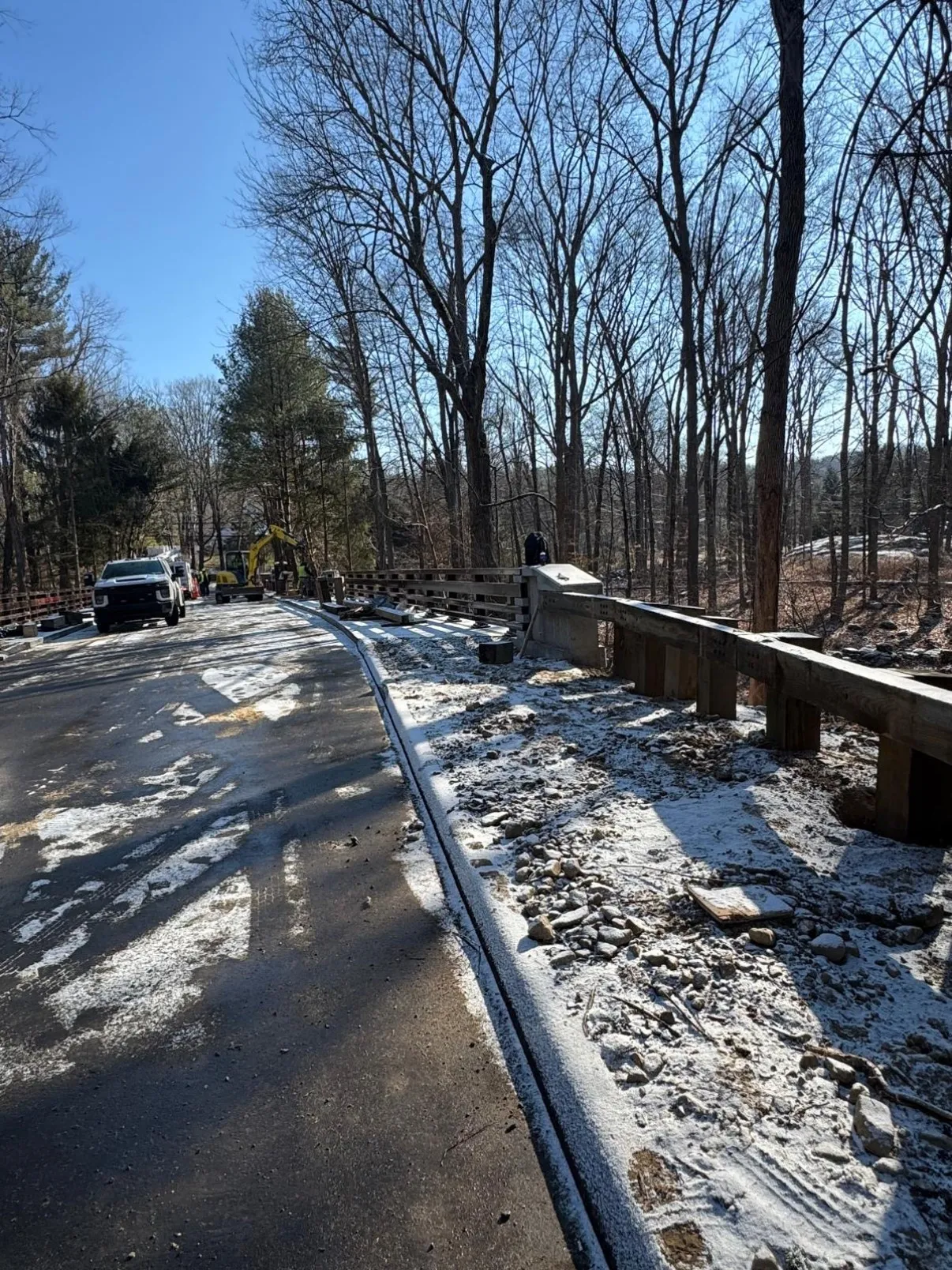 Winter bridge approach with a sealed deck, new concrete parapet and metal railing, and snow along the shoulder of the worksite