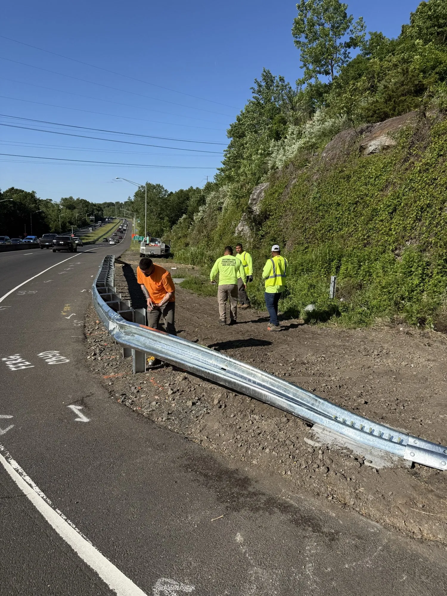 Crew installing fresh galvanized guardrail along a regraded highway shoulder