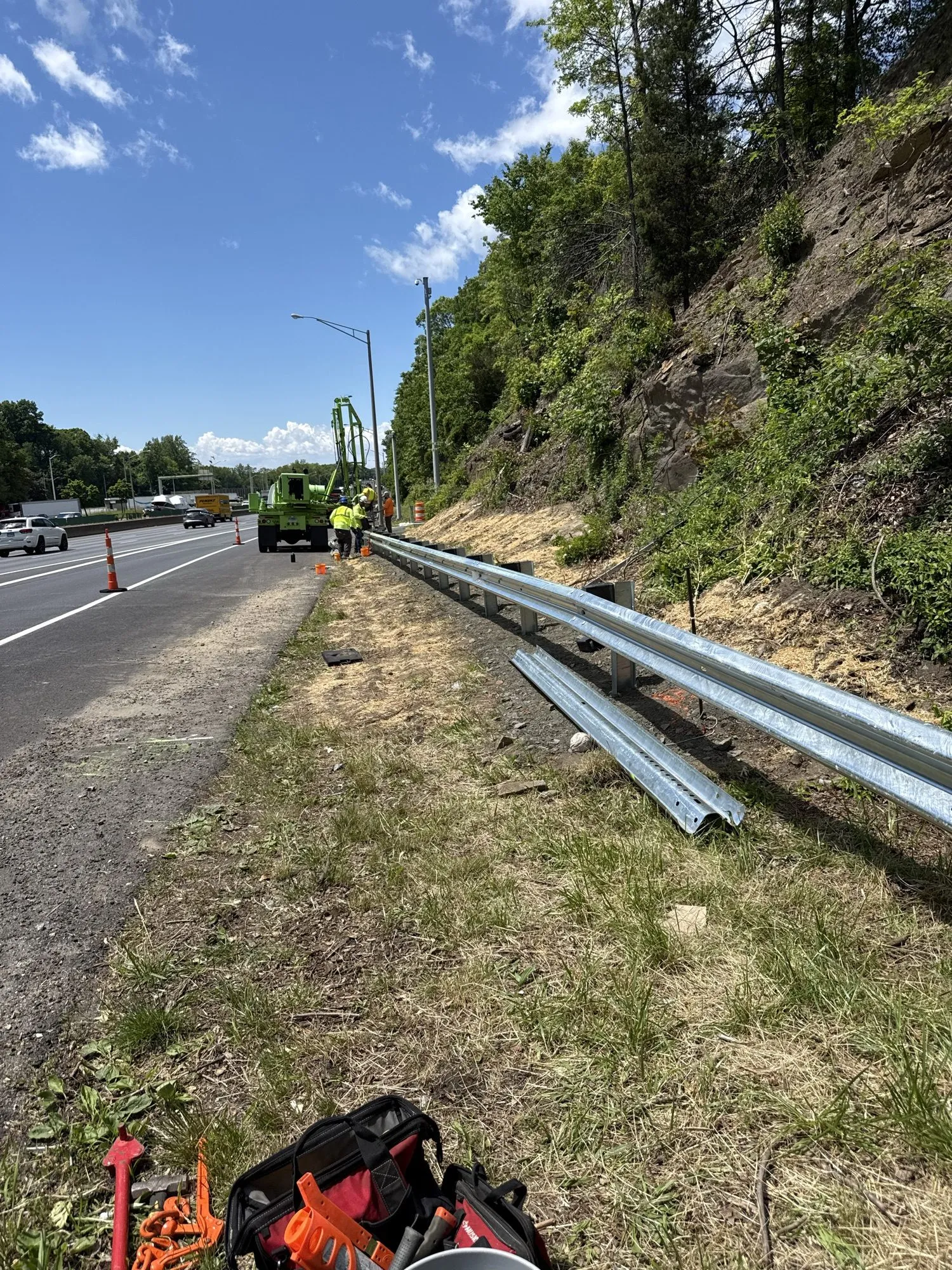 Hydraulic tracked post-driving rig and crew setting guardrail posts beside a highway