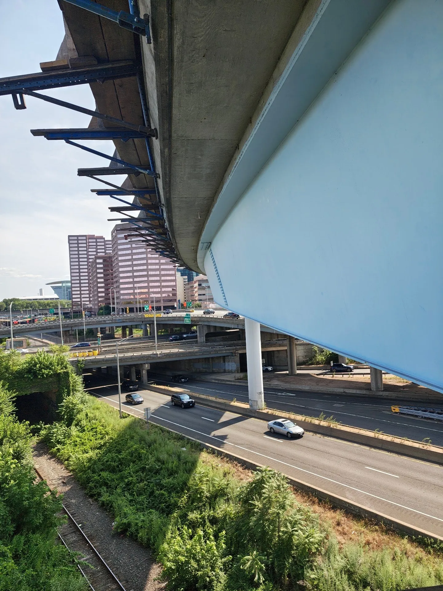 Recoated light-blue steel fascia girder on an elevated ramp at the I-84 and I-91 interchange in downtown Hartford, Connecticut, with the hung work platform beneath the deck