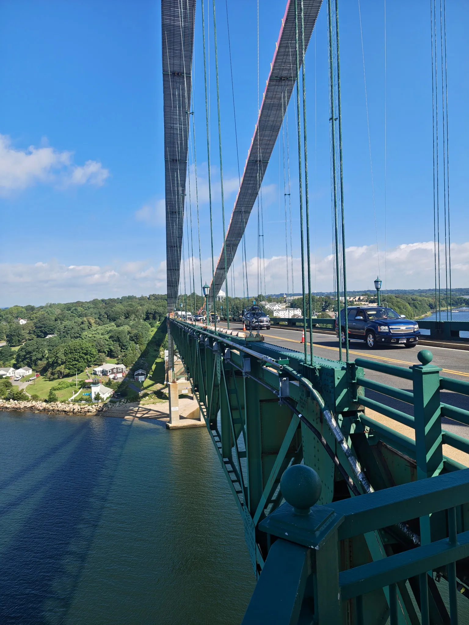 Mount Hope Bridge suspension span viewed along the deck from the tower, with newly painted green truss steel and railings, suspender cables, traffic crossing and a coned-off work zone in the travel lane