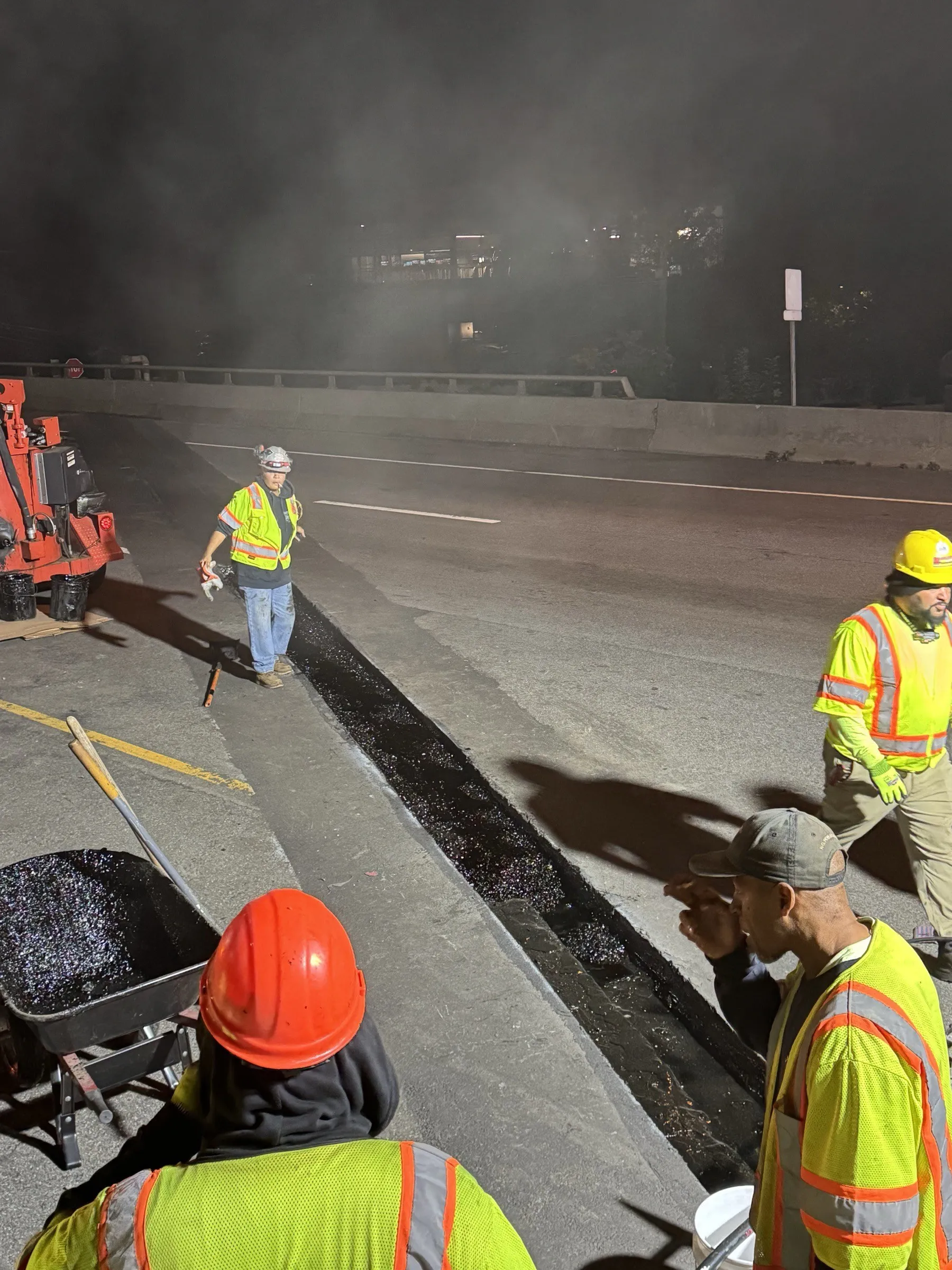 Cristiano & Son night crew working a bridge deck joint repair, multiple workers in hi-vis vests on a freeway overpass