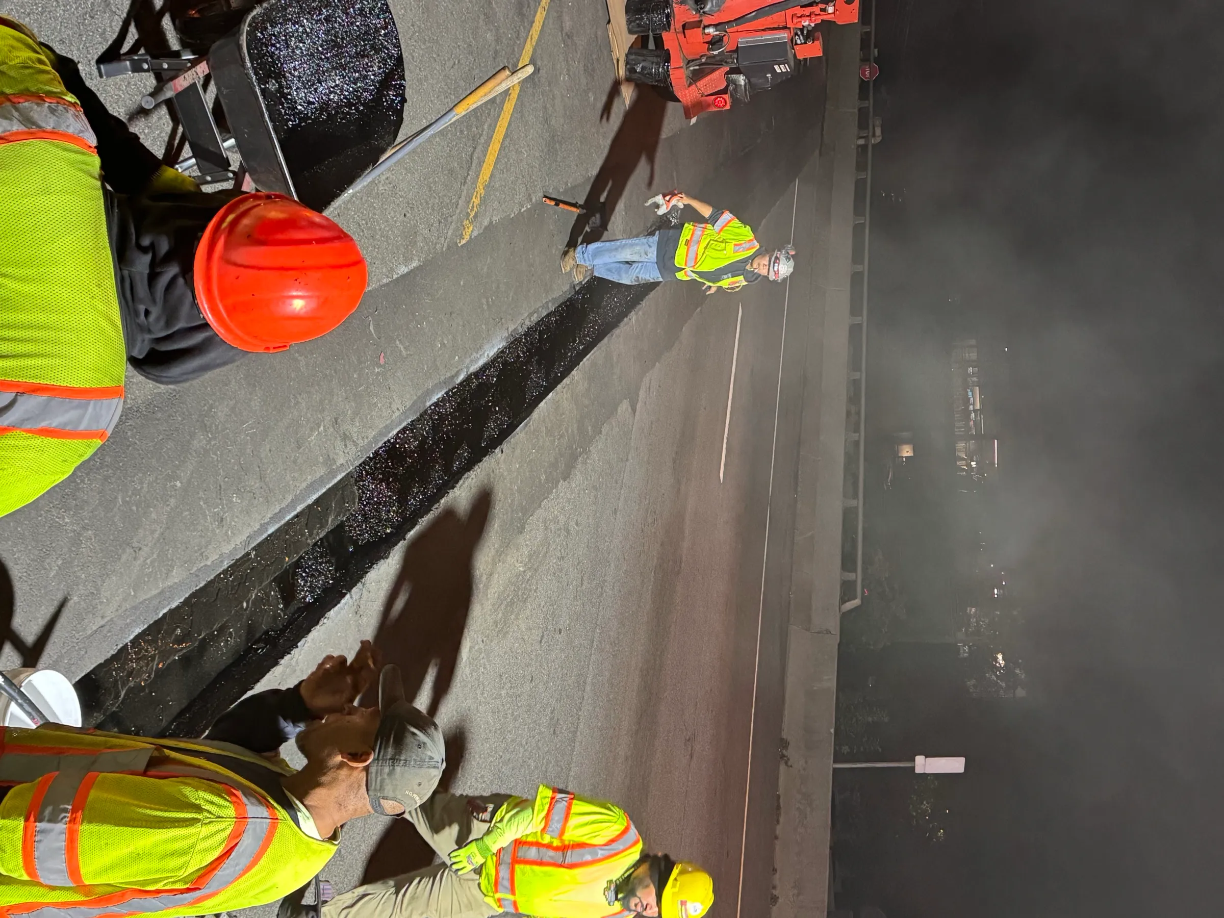 Cristiano & Son night crew working a bridge deck joint repair, multiple workers in hi-vis vests on a freeway overpass