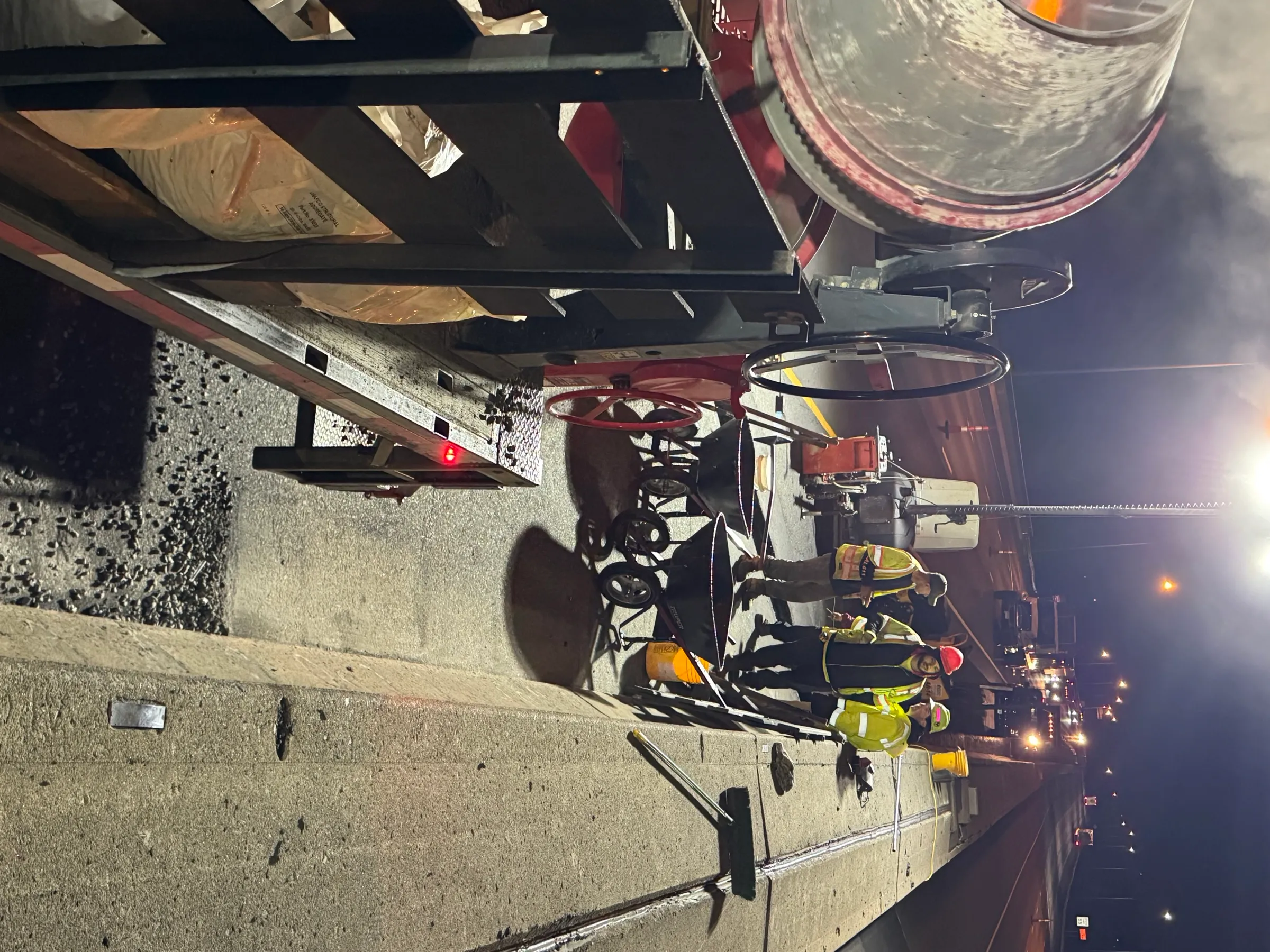 Three Cristiano & Son crew members coordinating on a Connecticut bridge deck at night with traffic in the distance