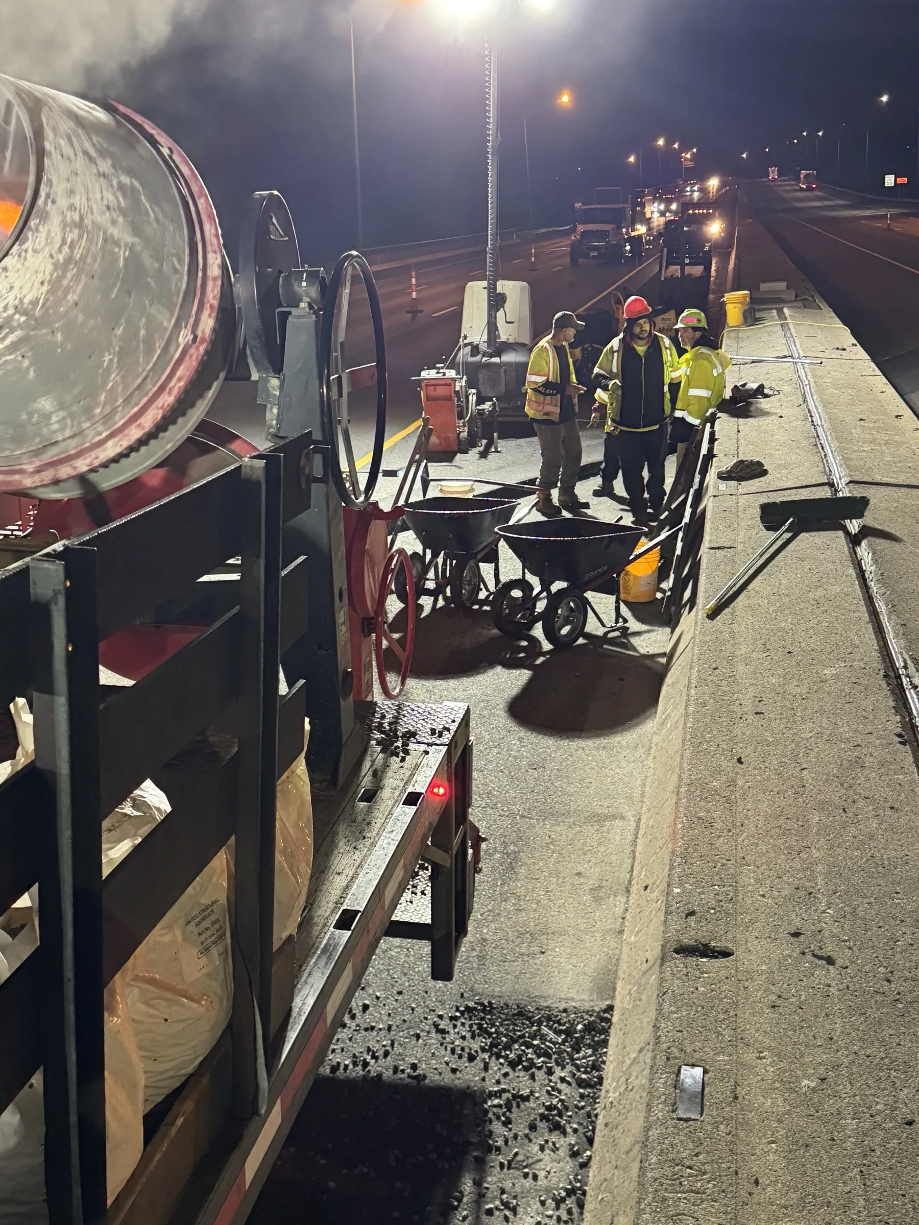 Three Cristiano & Son crew members coordinating on a Connecticut bridge deck at night with traffic in the distance