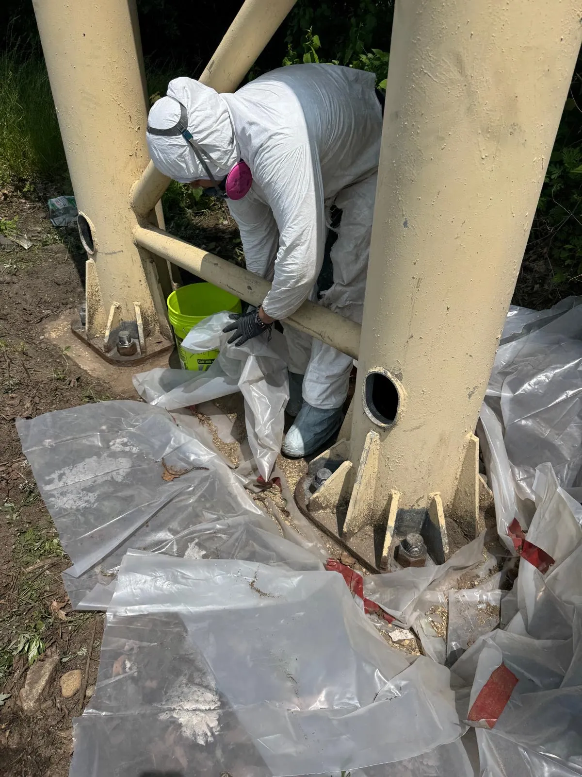 SSPC-certified technician in full containment suit and respirator working on a bridge column